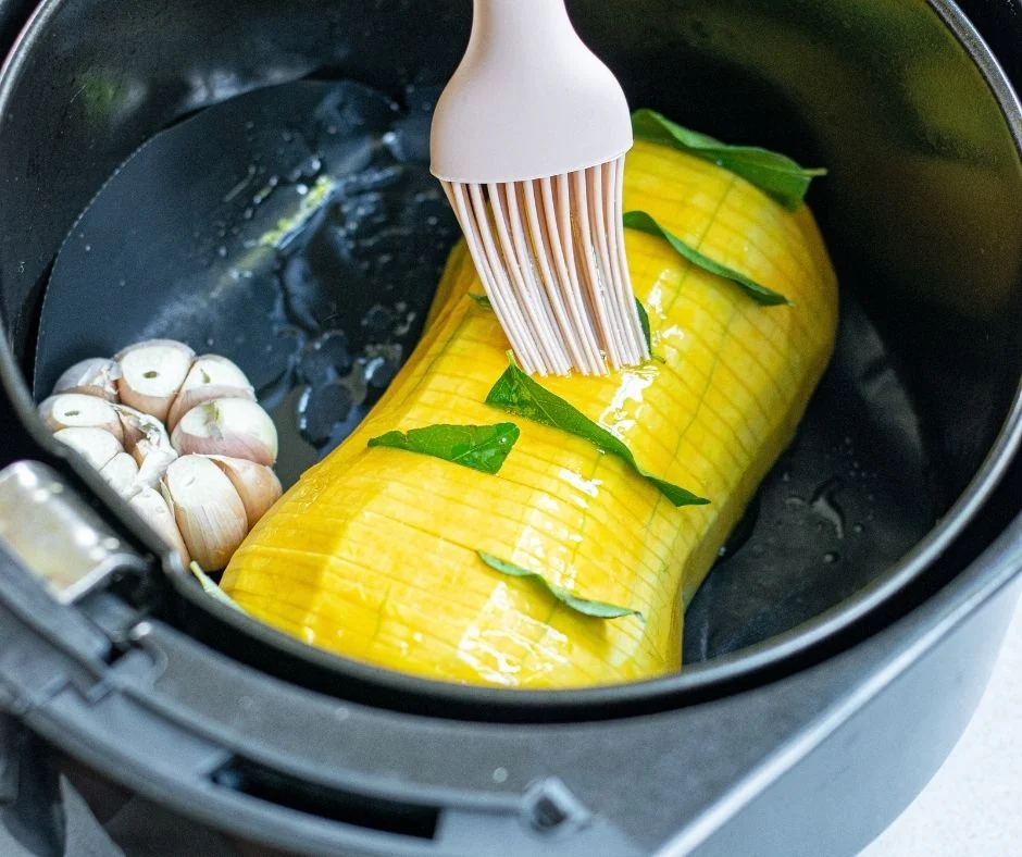 Hasselback Butternut Squash in air fryer basket, being brushed with olive oil
