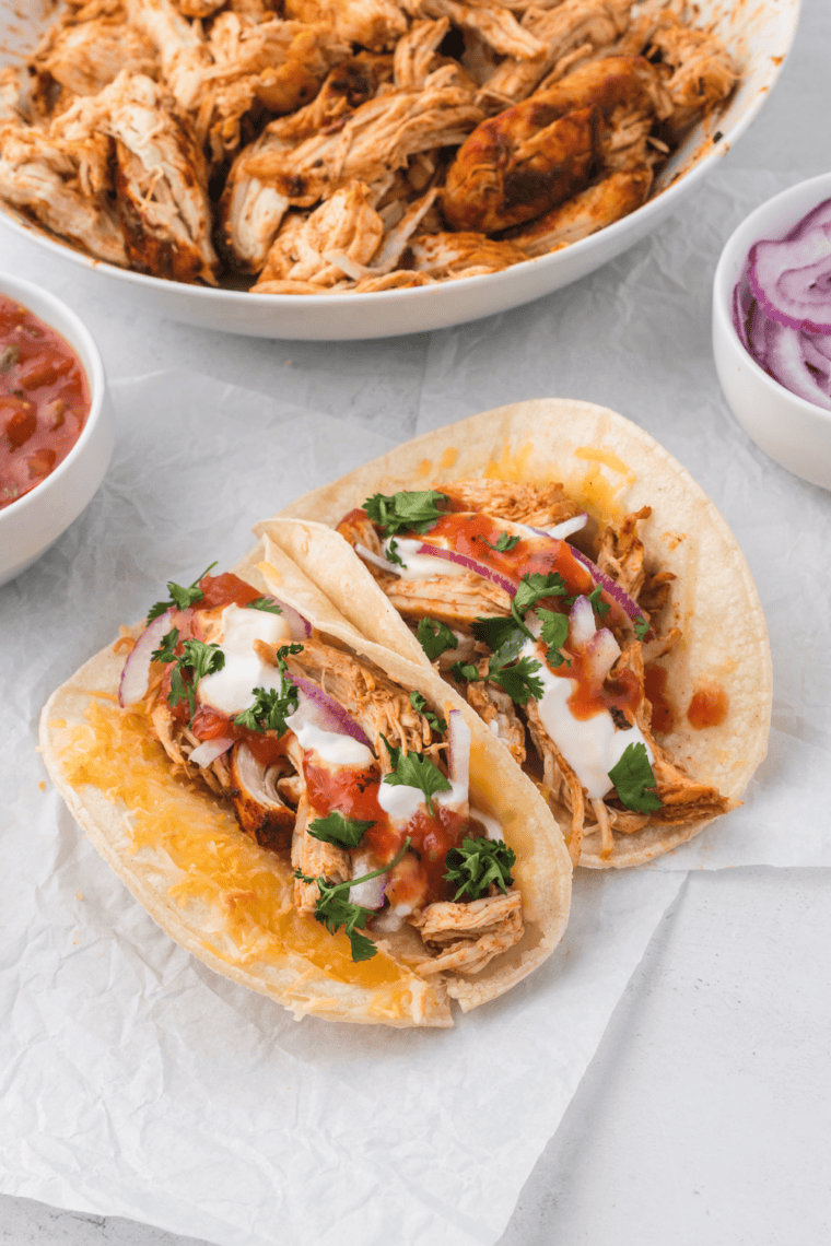 Three shredded chicken tacos topped with cilantro and diced onion