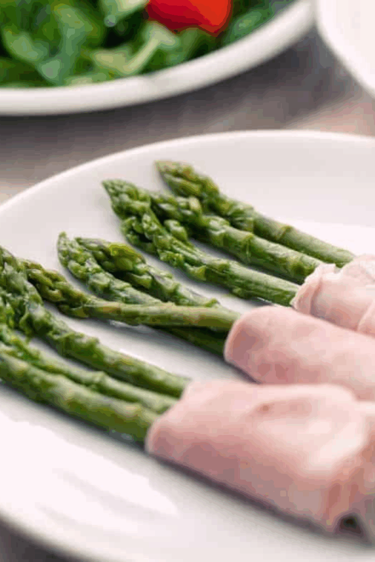 Ham-wrapped asparagus rolls on a serving plate, ready to eat