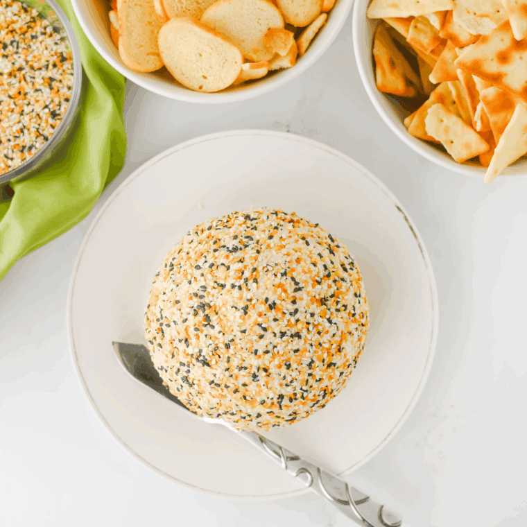 Everything Bagel Cheese Ball covered with bagel seasoning, served with crackers and fresh vegetables for a savory appetizer.