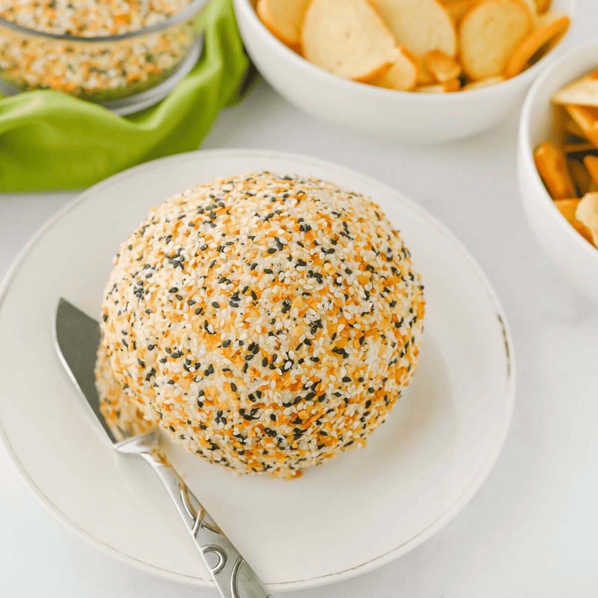 Everything Bagel Cheese Ball with creamy cheese, topped with everything bagel seasoning, served with crackers and veggies for dipping.