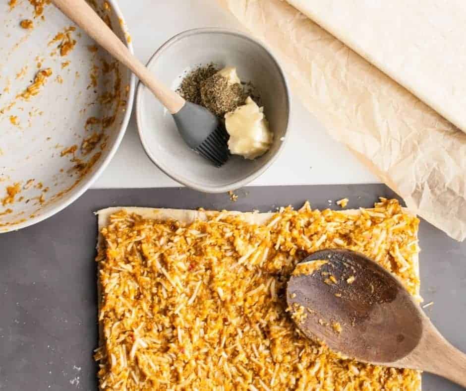 Savory pumpkin puree being spread evenly over a sheet of puff pastry with a spatula.