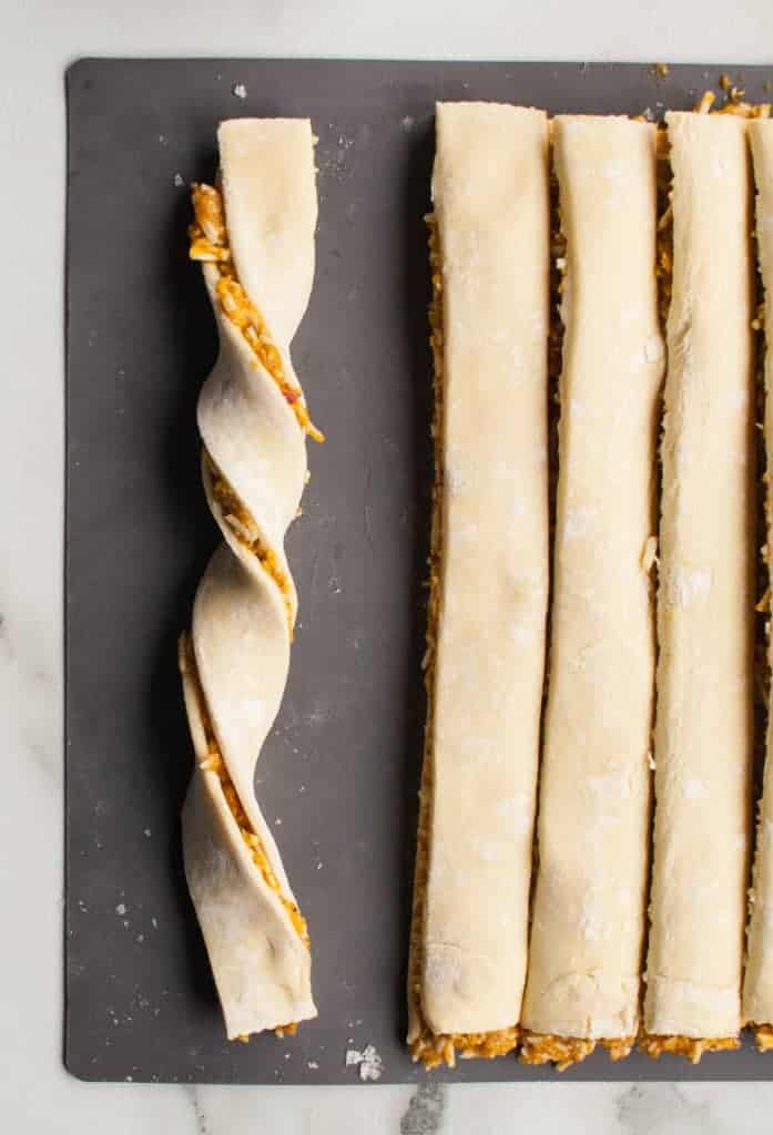 Hands twisting puff pastry strips filled with pumpkin, cheese, and pesto, preparing them for the air fryer.