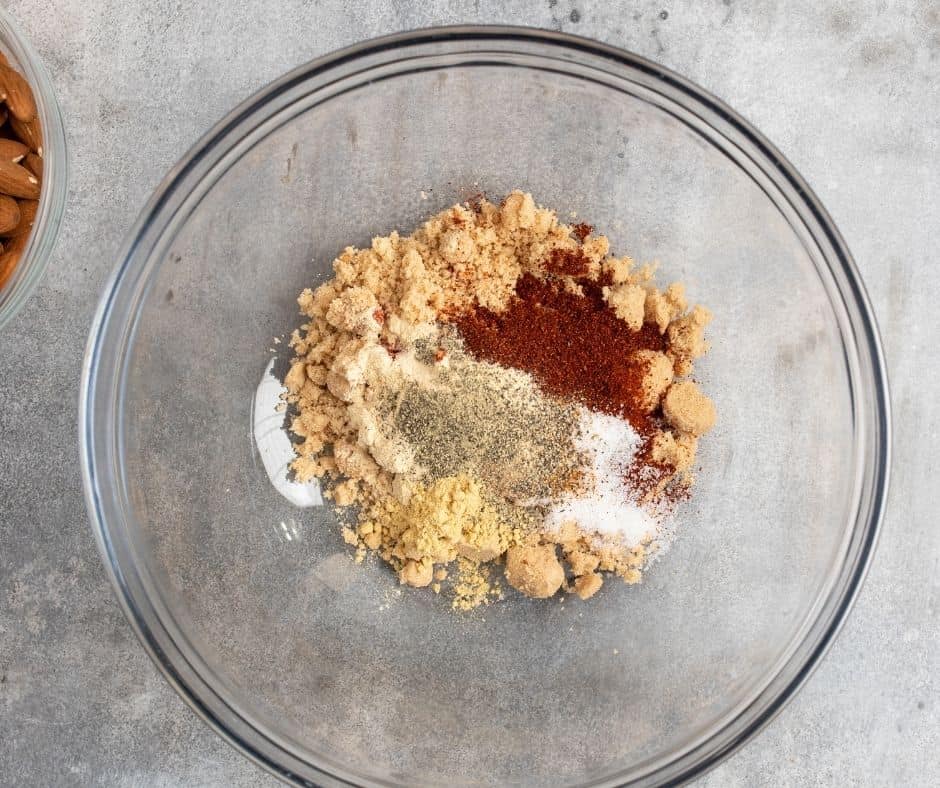 Spices including sweet paprika, smoked paprika, salt, black pepper, garlic powder, cayenne pepper, and mustard powder in a small bowl, with an egg white being whisked in a separate bowl.