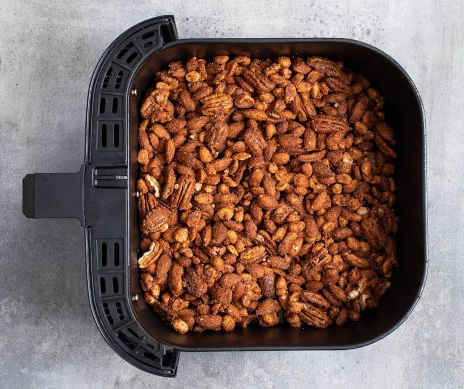 Spiced nuts spread evenly in the air fryer basket, cooking at 315°F for 8-10 minutes with frequent shaking.