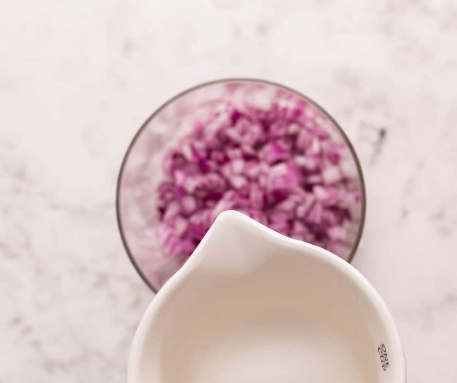 Pickled red onions in a mason jar with diced onions soaking in white vinegar for a tangy topping.