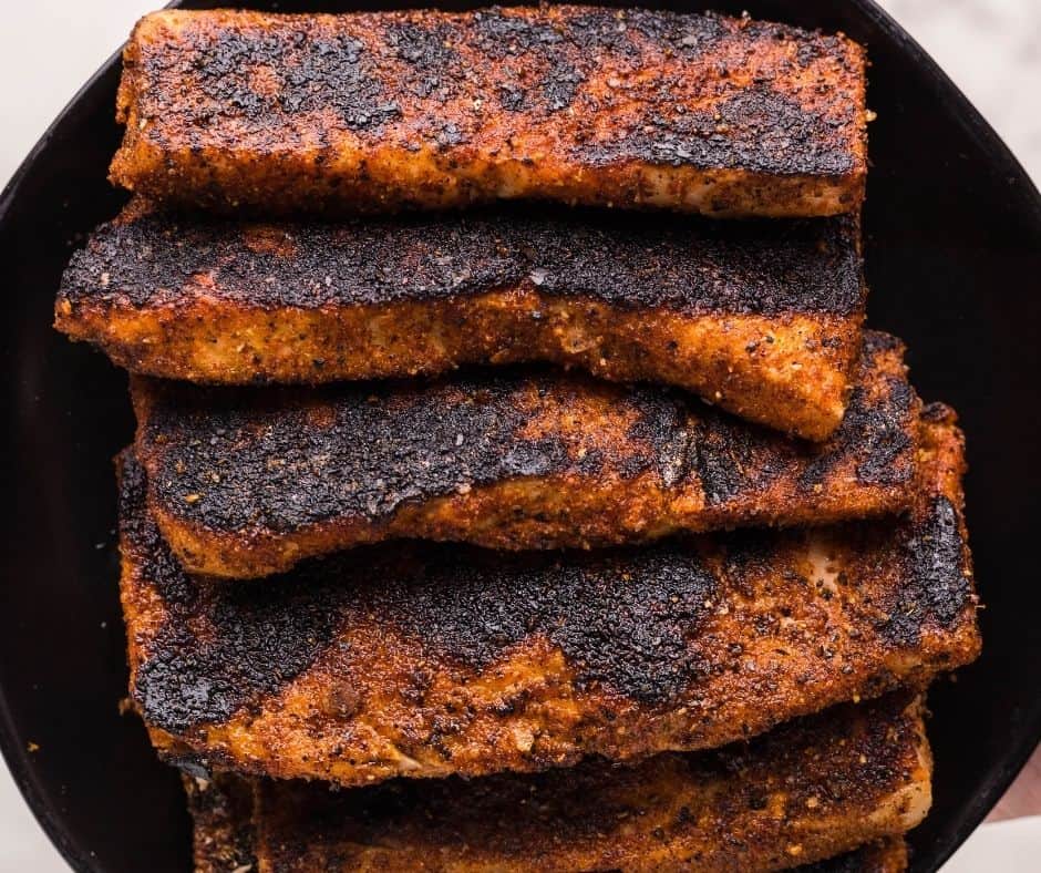 Blackened salmon searing in a hot skillet, coated with homemade seasoning, ready to be flaked for tacos.