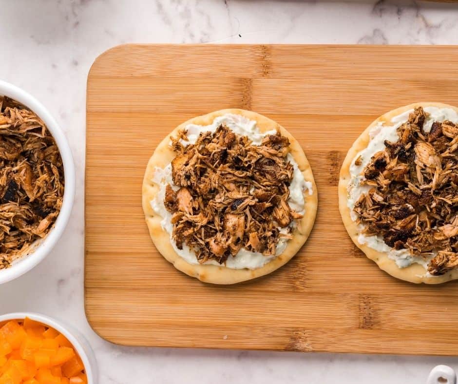 Naan topped with cream sauce and flaked salmon placed in an air fryer, ready to cook for a flavorful dish.