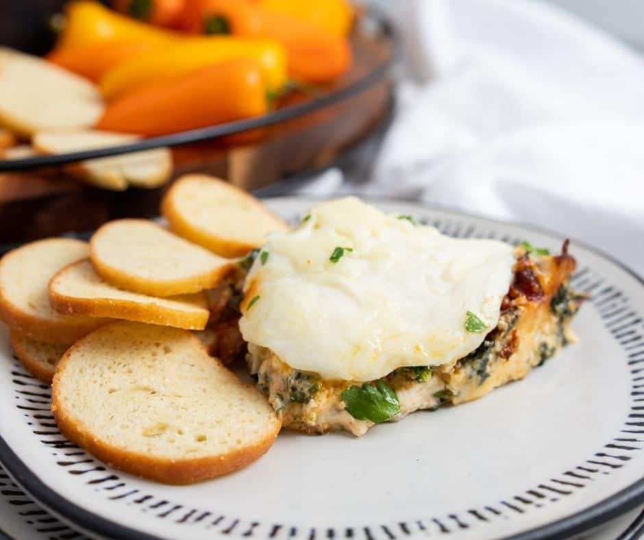 A golden, bubbly Air Fryer Cheesy Bacon Spinach Dip topped with melted cheese and crispy bacon, ready to be served in a white dish.