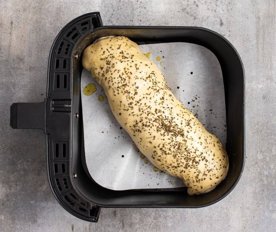 Place the pizza bread in a parchment or silicone-lined air fryer basket, brush with olive oil, season with dried oregano, and cook at 320°F for 10-15 minutes, flipping halfway if necessary.