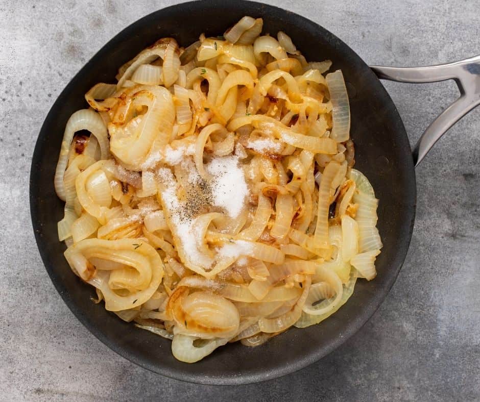Caramelized onions in a skillet with sugar, salt, black pepper, and balsamic vinegar cooking until the liquid evaporates.