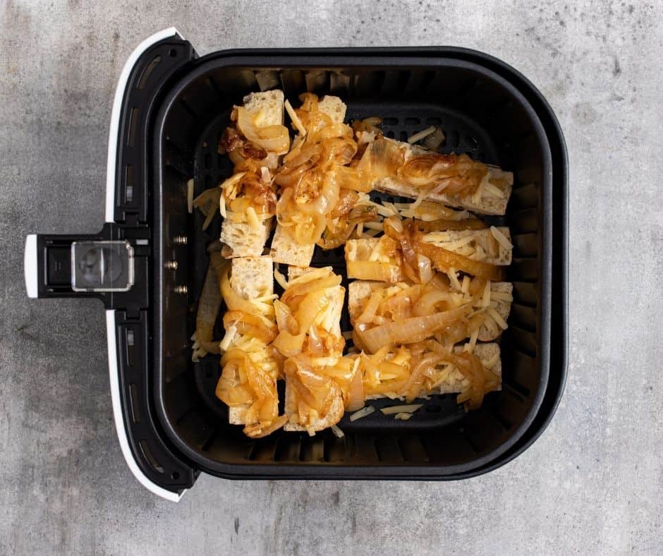 Sliced bread topped with cheese and caramelized onion mixture, ready to be air fried until the cheese melts.