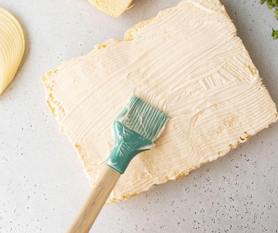 Spray a pan with cooking spray, place the bottom halves of slider rolls in the pan, and spread mayonnaise over the top.