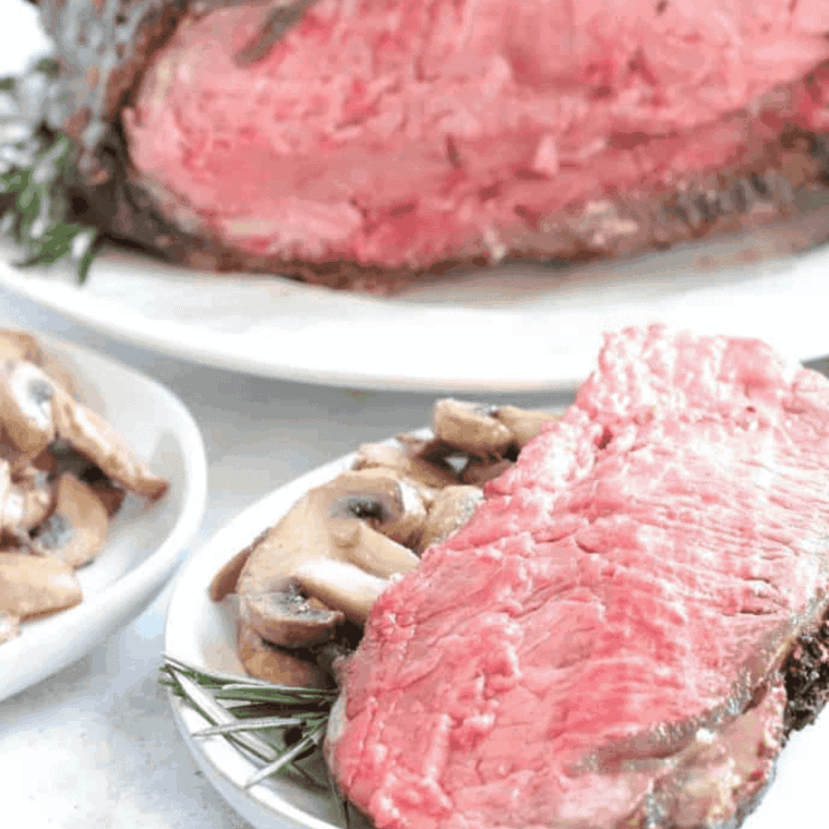Sliced Air Fryer Prime Rib roast showing a perfect pink medium-rare center, a dark garlic-herb crust, and resting on a cutting board.
