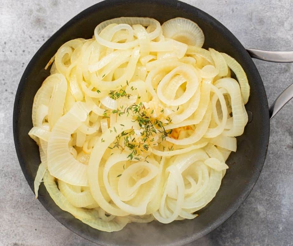 Skillet with melted butter, onions, garlic, and thyme simmering to caramelize for French Onion Cheese Bread.