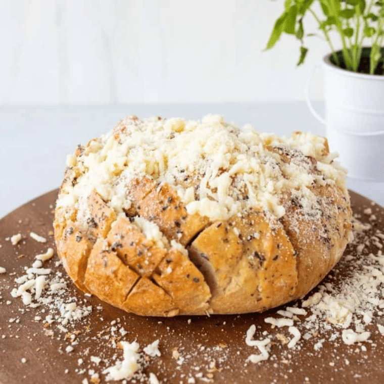 Shredded cheese mixture being added to sliced bread cavities, with melted butter drizzled on top, and the loaf wrapped in aluminum foil.