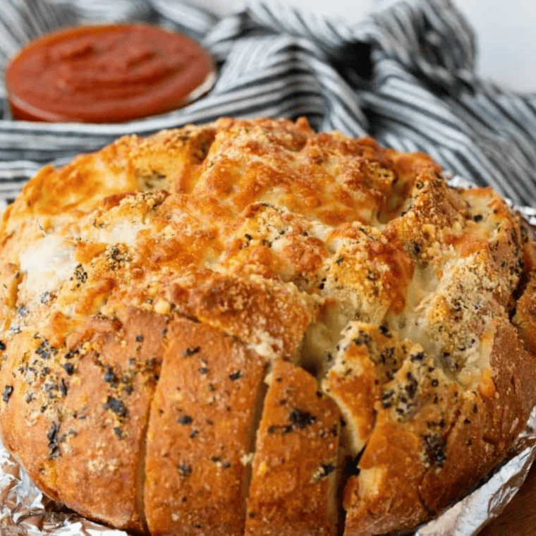 Air fryer basket with foil-wrapped bread cooking at 320 degrees, later unwrapped and topped with melted cheese, served alongside marinara sauce.
