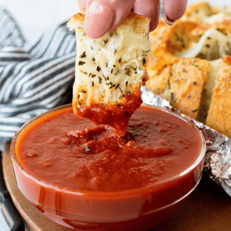 Air Fryer Mozzarella Pizza Bread with golden, melted cheese and marinara sauce on the side, served on a wooden board.