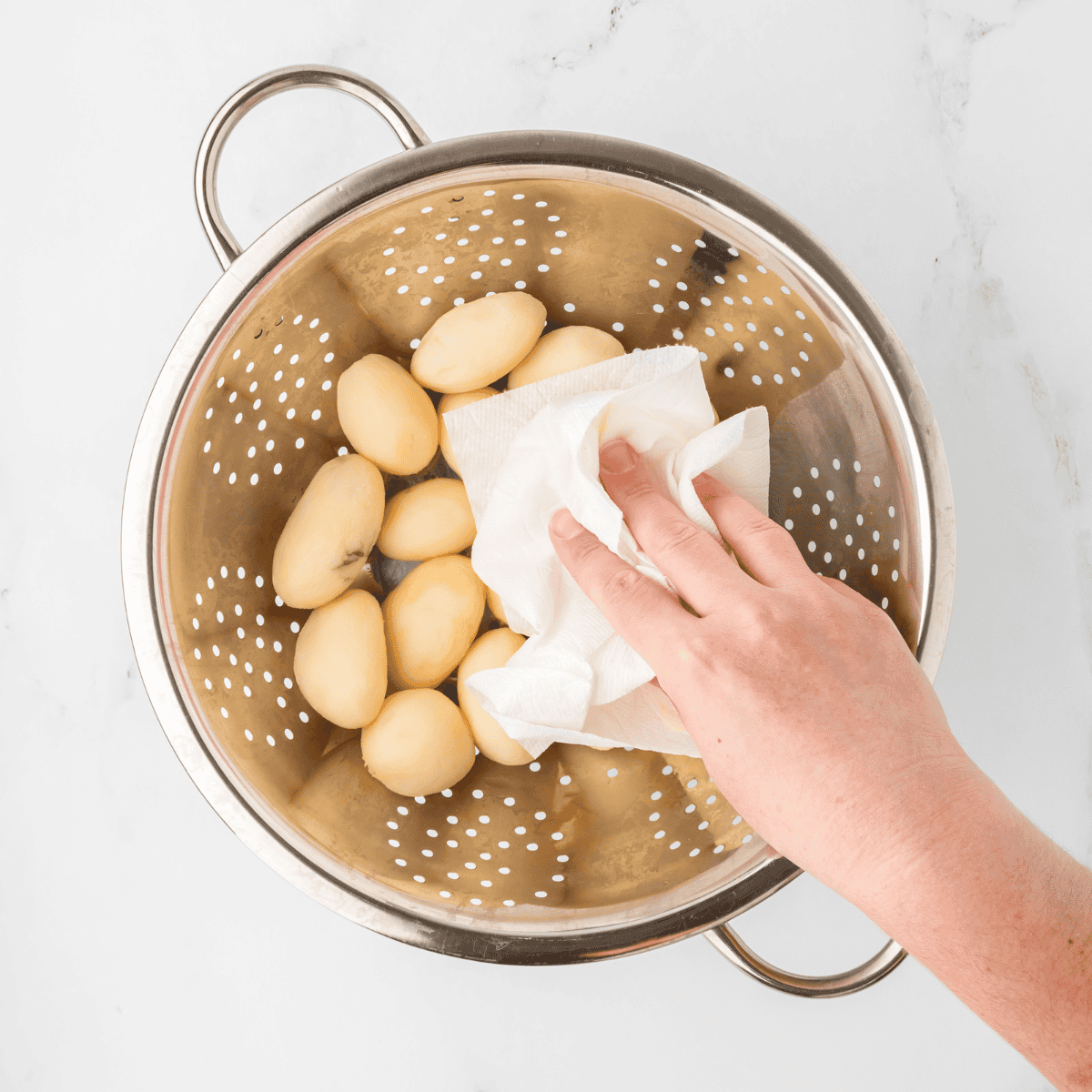 Drained and rinsed canned potatoes being patted dry with paper towels to remove excess moisture for perfect air frying crispiness.