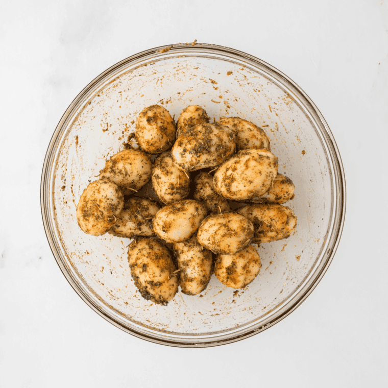 Dried canned potatoes in a bowl, drizzled with olive oil and seasoned with salt, black pepper, and spices, ready to be tossed.