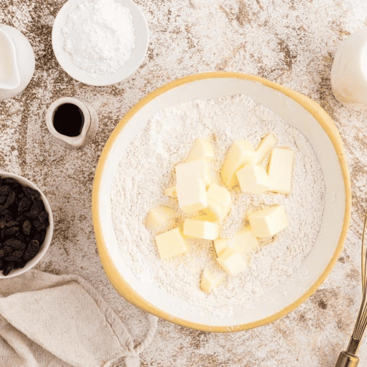 Sifted flour, sugar, baking powder, baking soda, salt, and cinnamon in a bowl with cold butter cut into pea-sized pieces, ready for mixing.