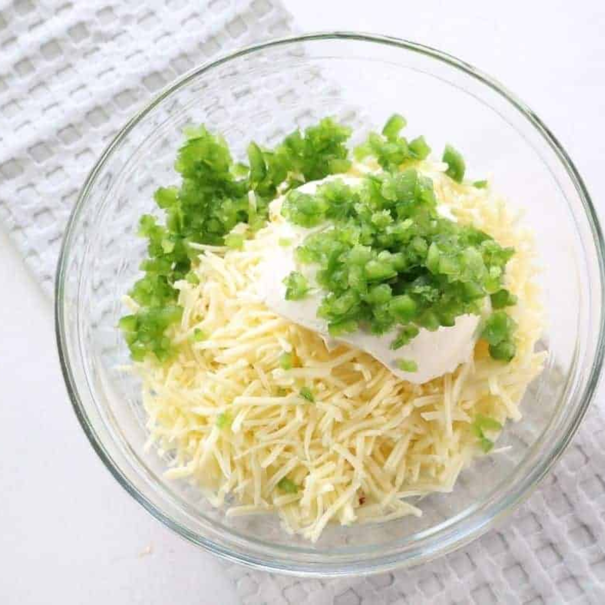 Mixing shredded cheese, cream cheese, and diced jalapeƱos in a bowl