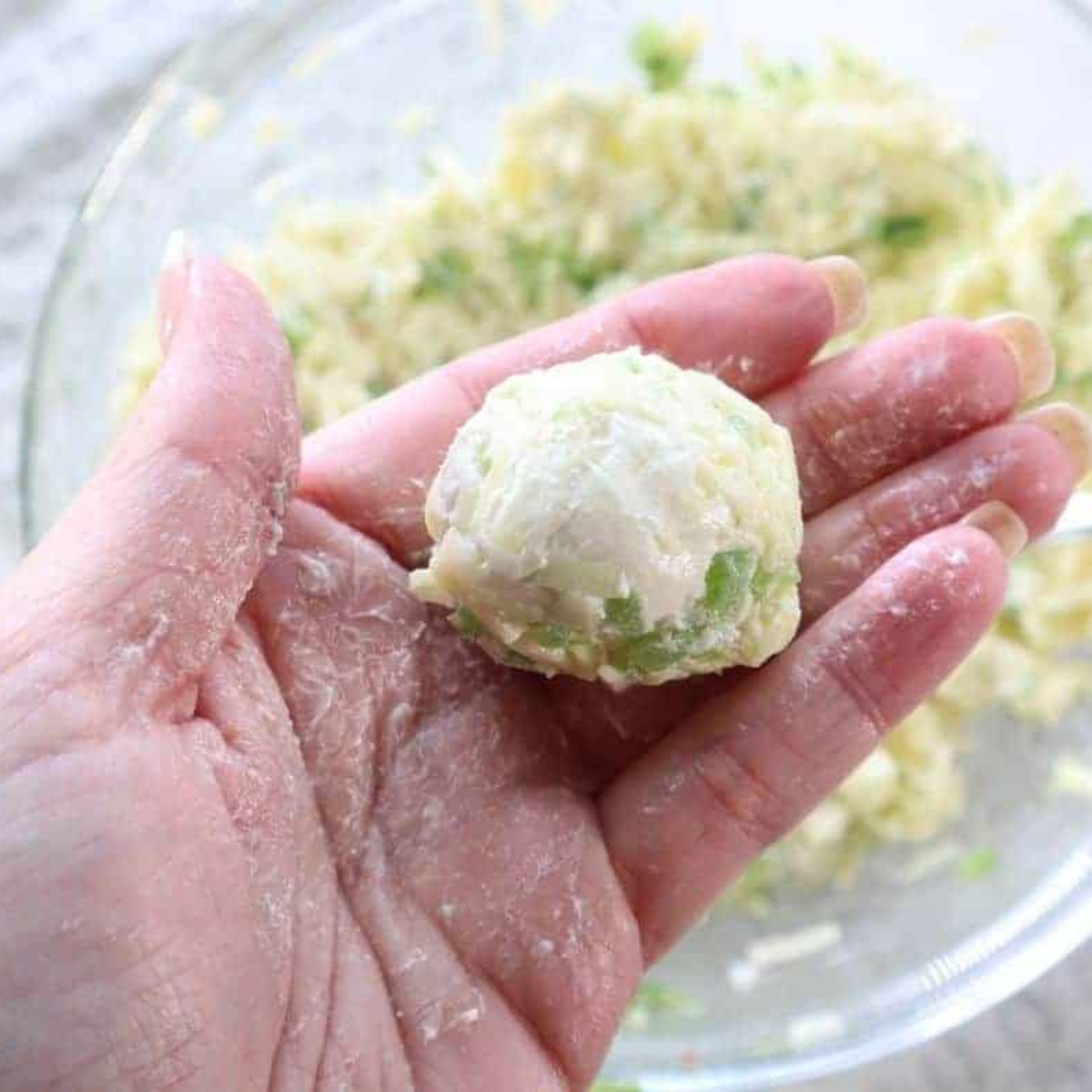Forming cheese and jalapeƱo mixture into balls using hands