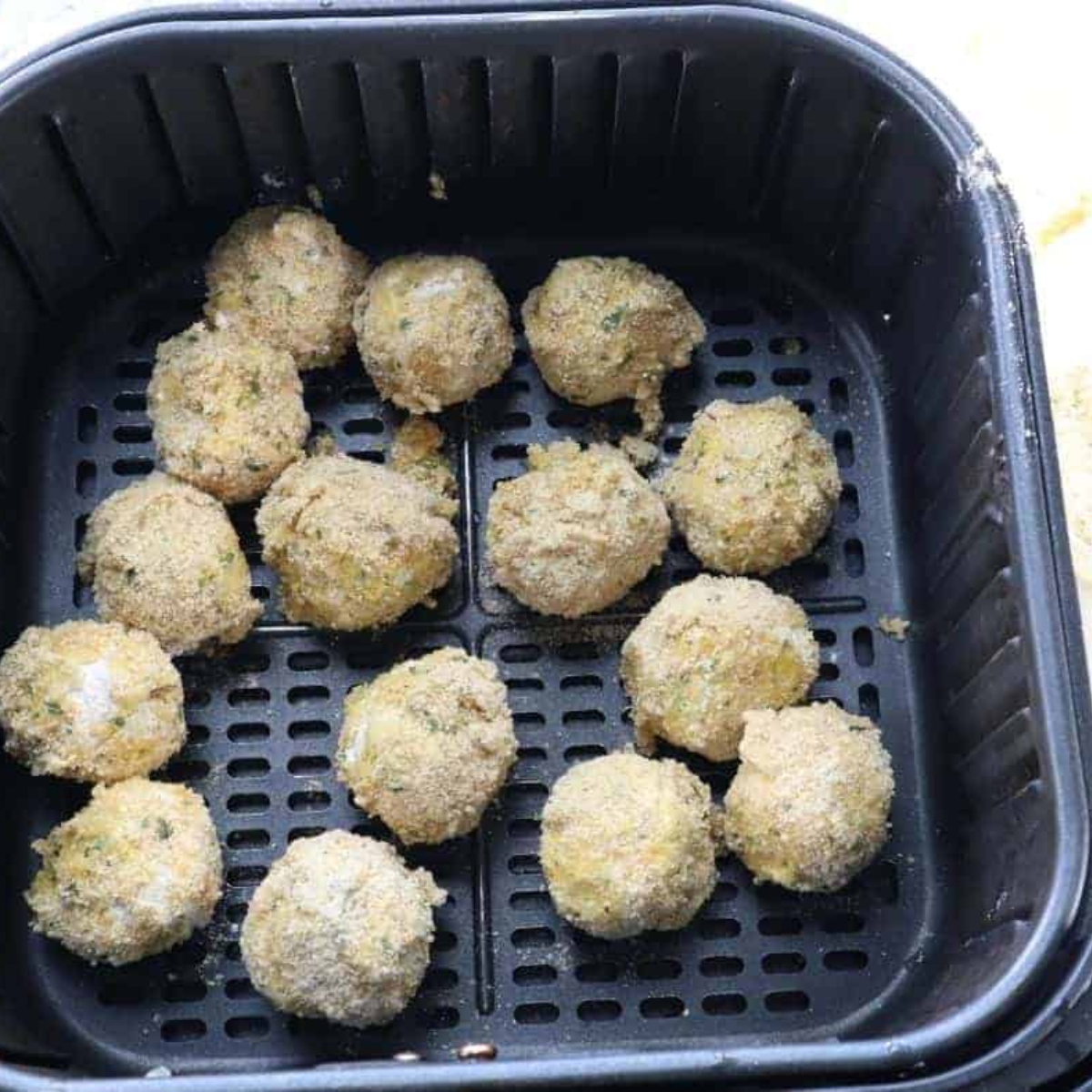 Spraying air fryer basket with cooking spray and placing cheese balls inside