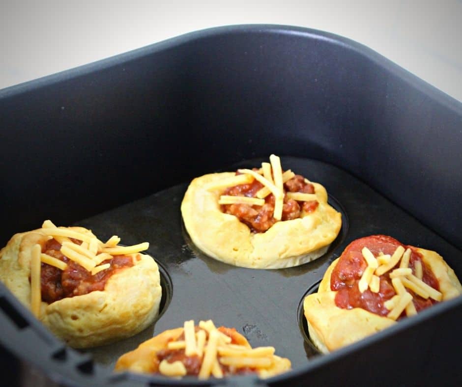 Sloppy Joe mixture spooned into biscuit cups, topped with shredded cheese, ready for air frying until melted.