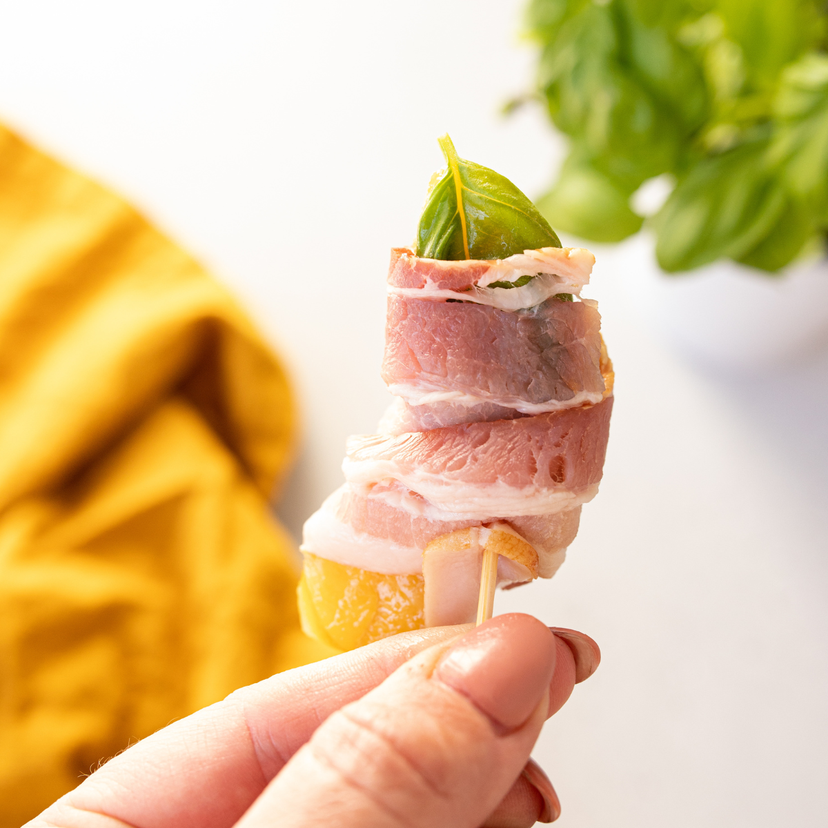 Fresh or canned peaches wrapped with bacon and a basil leaf, secured with a toothpick, ready to be placed in the air fryer basket.