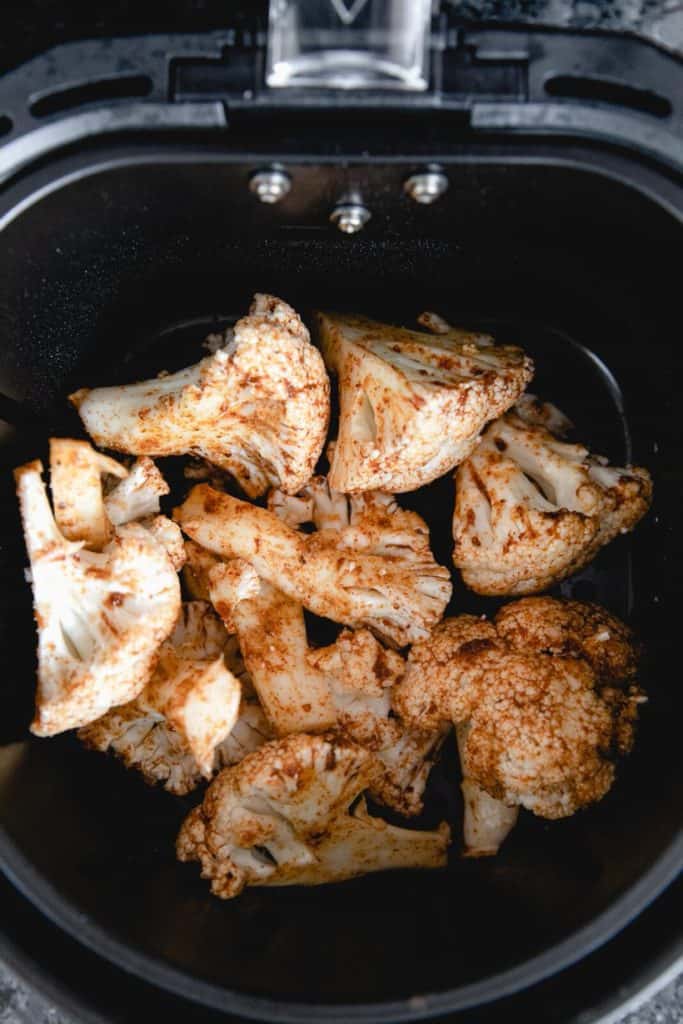Seasoned cauliflower florets in a single layer in the air fryer basket