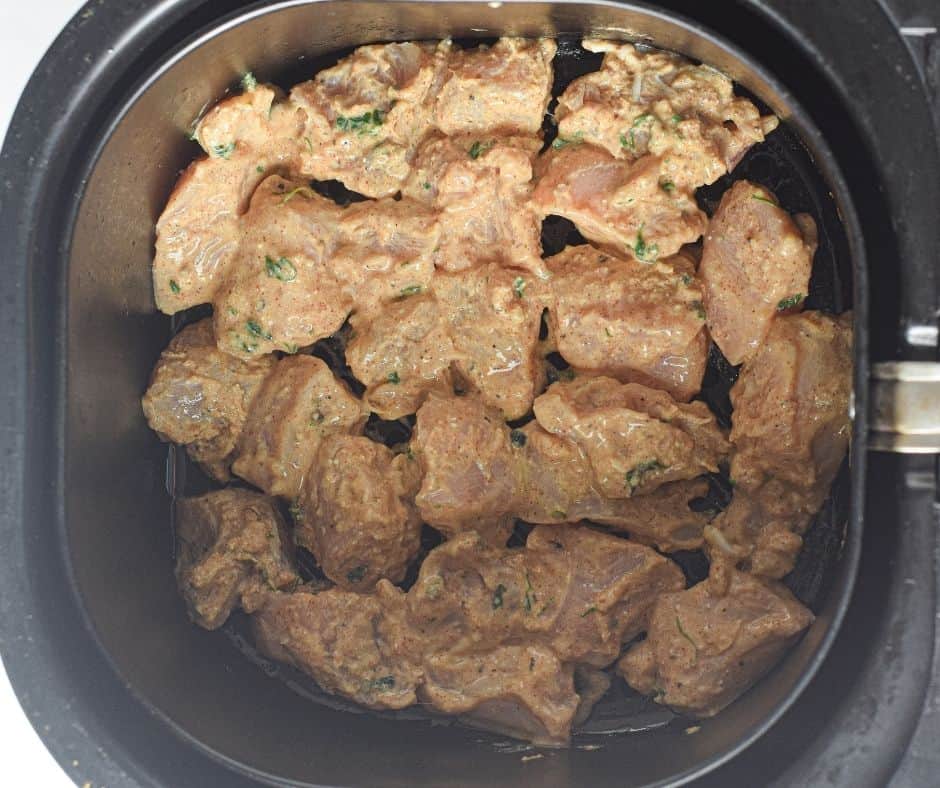 Marinated chicken pieces with bell peppers and onions in an air fryer basket, brushed with butter, cooking to a golden-brown finish.