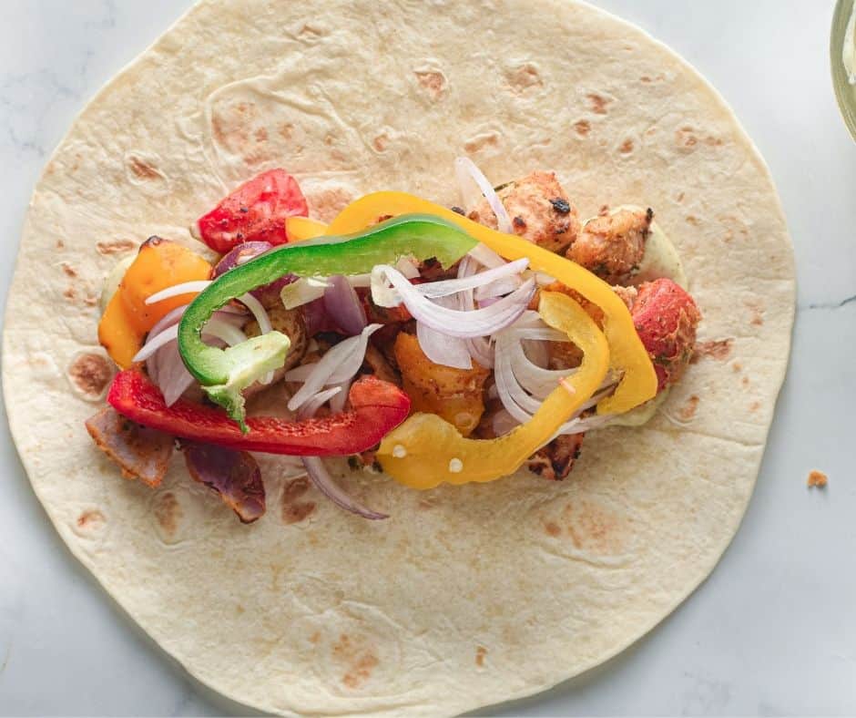 Assembled Chicken Tikka Tortilla Wrap with air-fried bell peppers, onions, lettuce, and creamy mayo-mint chutney, ready to roll.