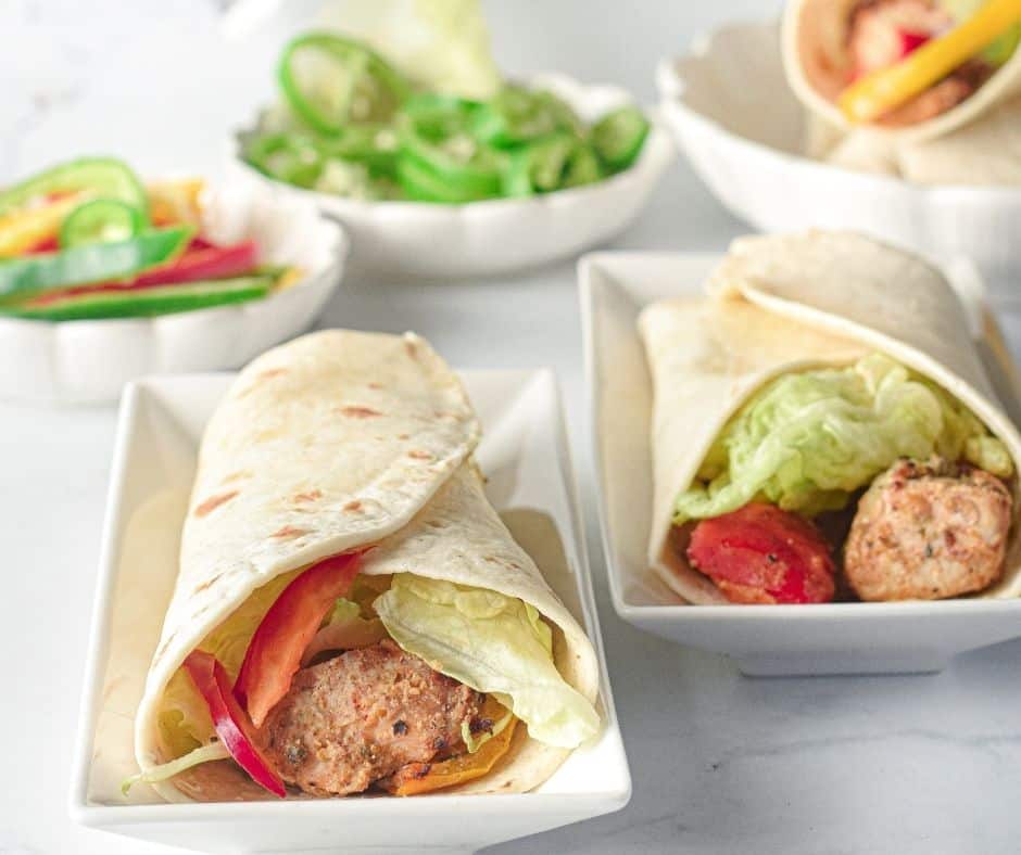 Easy Air Fryer Chicken Tikka Tortilla Wraps sliced in half, filled with spiced chicken, bell peppers, onions, lettuce, and drizzled mint-mayo sauce.