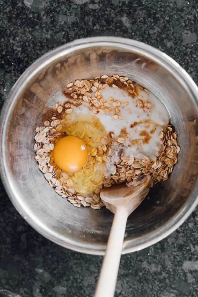 Oats, cinnamon and egg combined in a mixing bowl to make cinnamon roll baked oatmeal batter