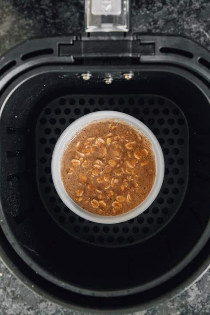 Ramekin of cinnamon roll oatmeal batter placed in the air fryer basket before baking