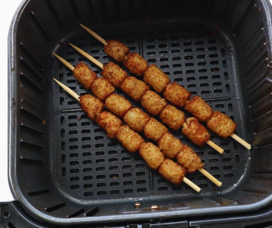 Crispy tater tots cooling on a tray next to soaked wooden skewers, ready to be threaded for loaded tater tot skewers.