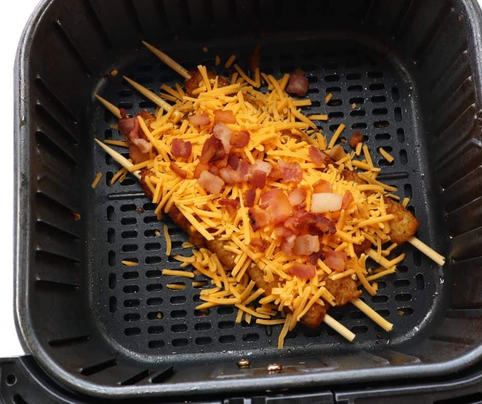 Tater tot skewers topped with shredded cheese and crumbled bacon placed in the air fryer at 300°F until the cheese melts perfectly.