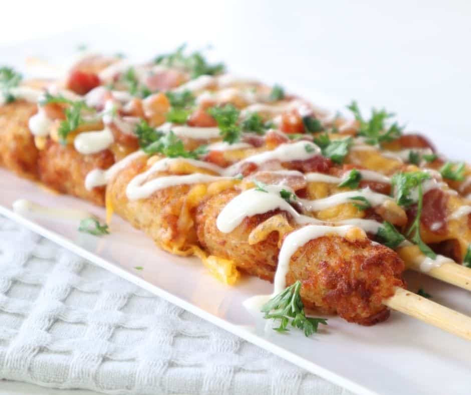 A plate of crispy Air Fryer Loaded Tater Tot Skewers topped with melted cheese, crispy bacon, and garnished with green onions, ready to serve.