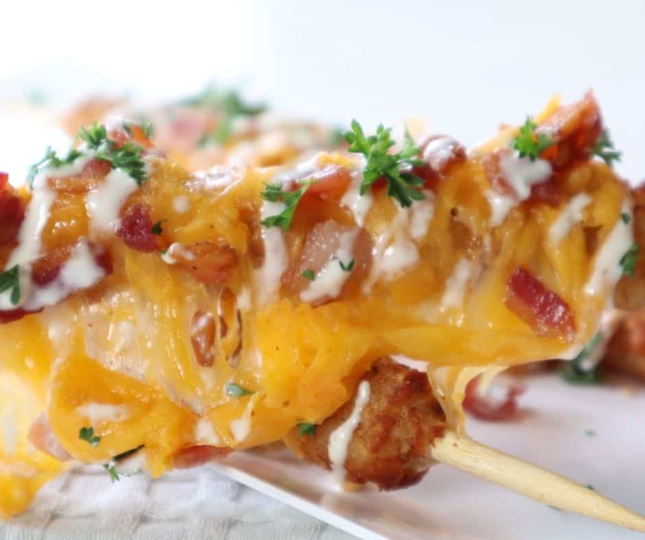 Crispy Air Fryer Loaded Tater Tot Skewers on a plate, topped with melted cheese, bacon, and green onions, ready to enjoy.