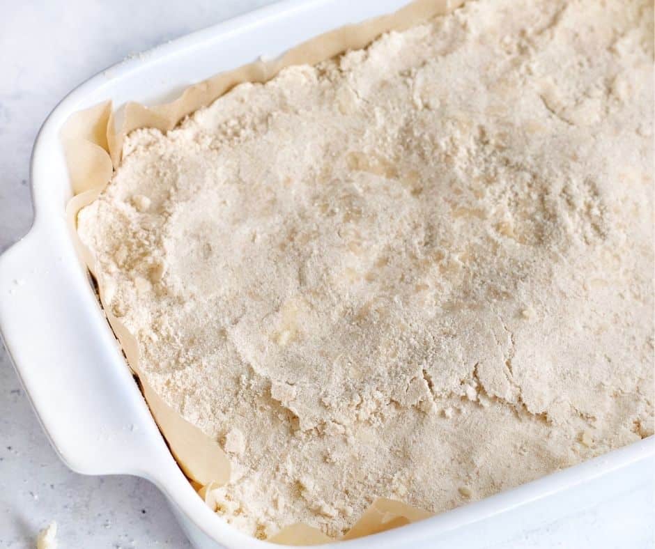 Mixing the ingredients with a beater or fork, mashing butter, and pressing the mixture evenly into the parchment-lined baking dish for Air Fryer Maple Pecan Bars.