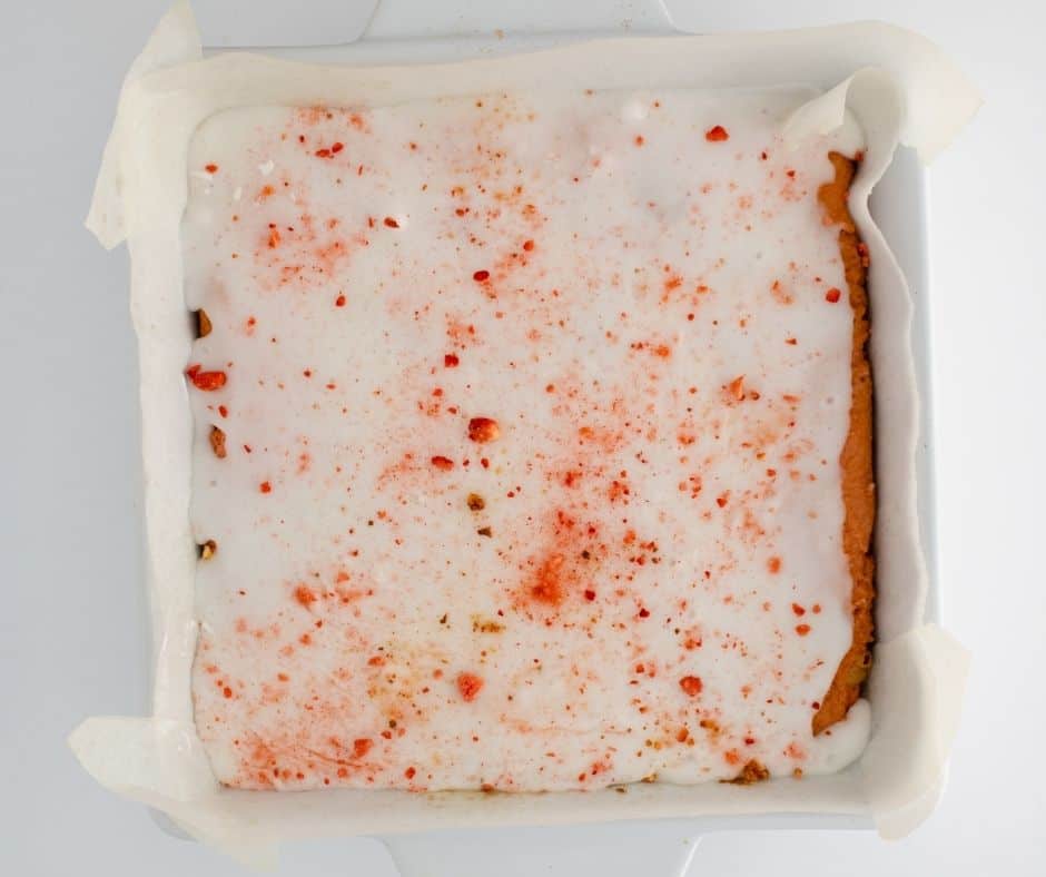 Vanilla glaze being poured over cooled air fryer strawberry blondies