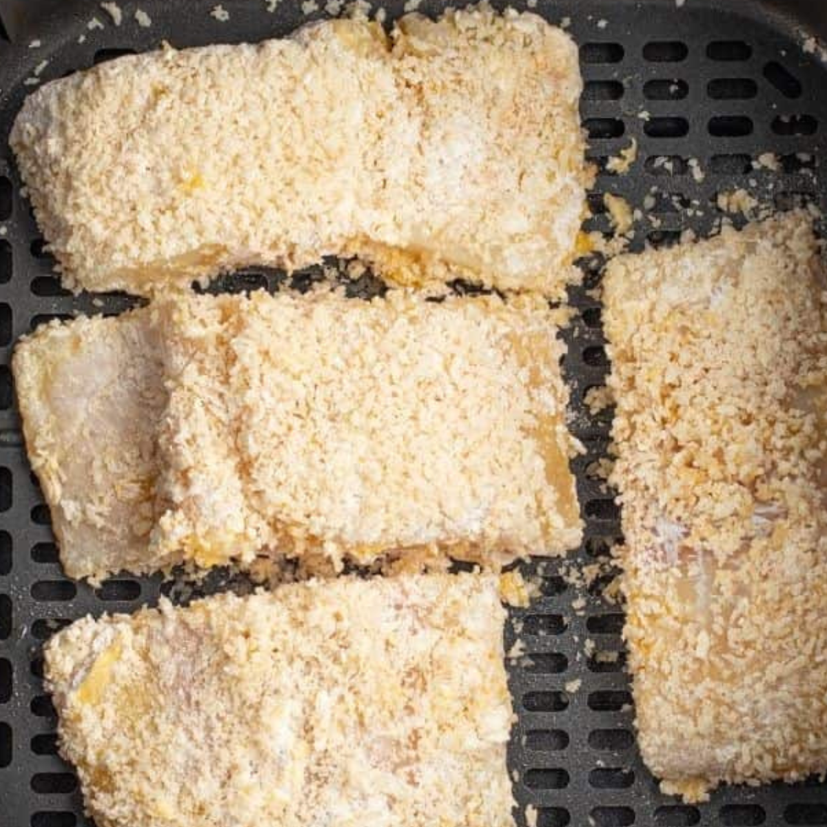 Air fryer cod fillets cooking to golden brown perfection with a crispy coating, ready to flake easily with a fork.