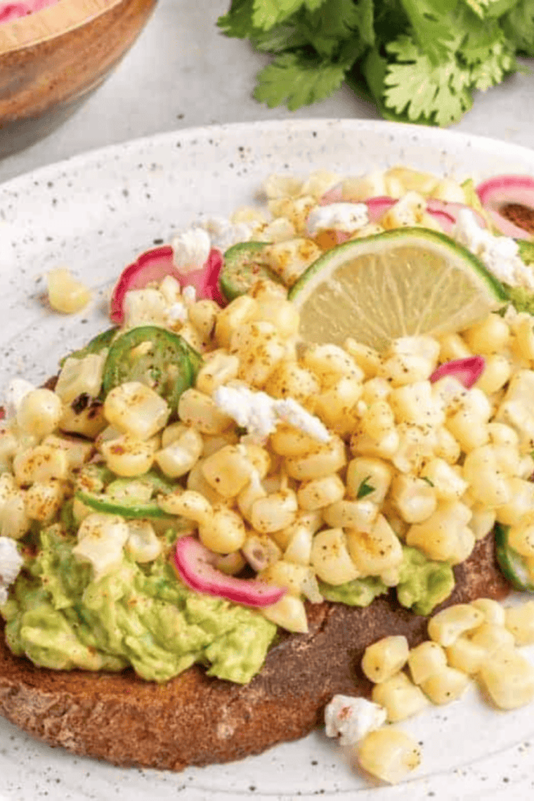 air fryer elote avocado toast topped with cheese, corn, lime, and cilantro