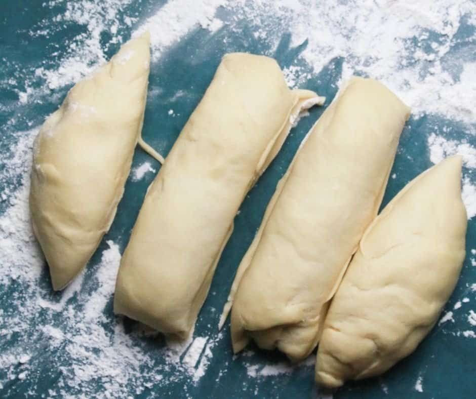 Dough being removed from the bowl onto a floured surface, cut into fourths, and rolled into rectangles with folded sides, then rolled from the short side to shape the dough.