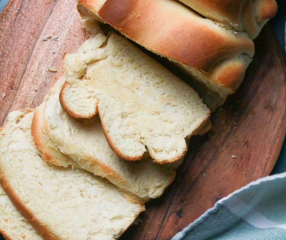 Golden-brown Air Fryer Milk Bread loaf sliced and served on a wooden board with a pat of butter.