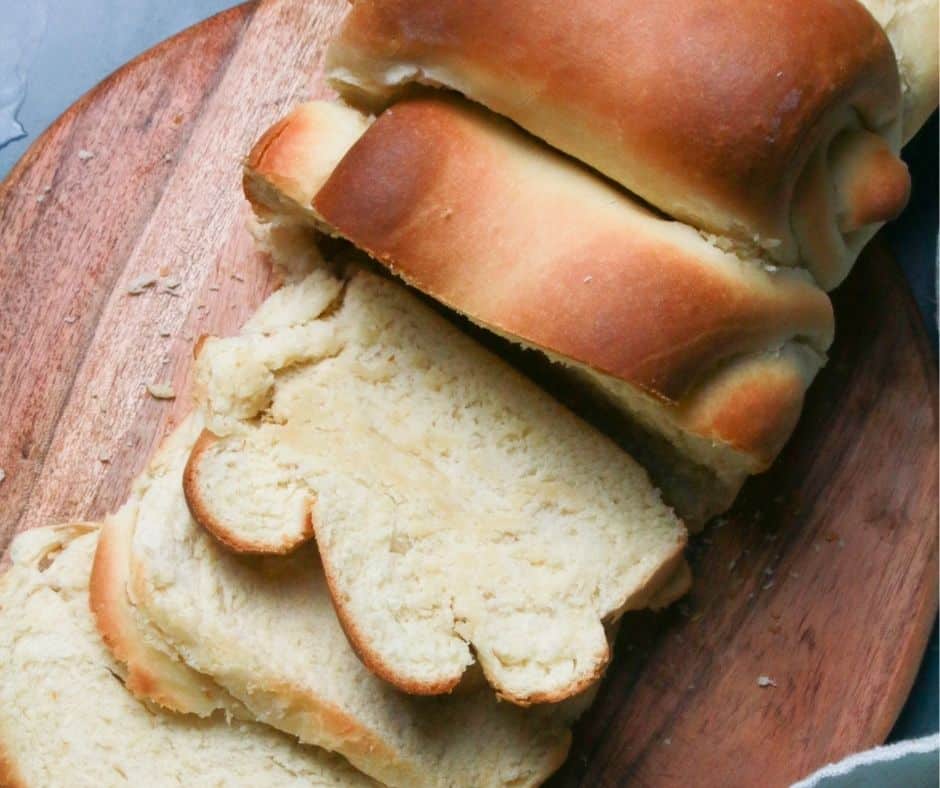 Golden-brown and fluffy Air Fryer Milk Bread loaf, sliced and served on a wooden board with a pat of butter.