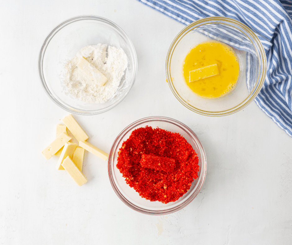Setting up separate bowls with flour, beaten egg, and crushed Takis for coating the mozzarella sticks.
