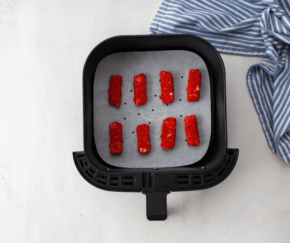 Arranging coated mozzarella sticks in the air fryer basket, spraying with oil, and cooking at 375°F for 6-8 minutes until golden and crispy.