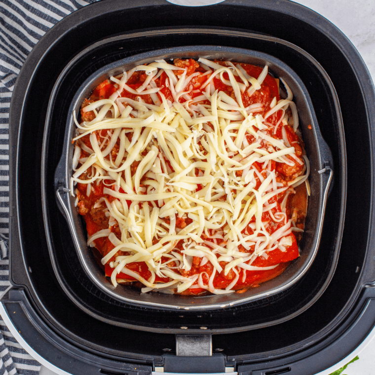 Sprinkling shredded mozzarella cheese over sauce layer while assembling air fryer lasagna